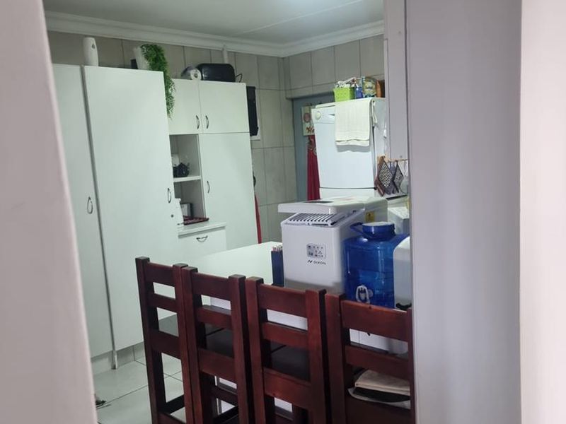 A functional kitchen area featuring built-in white cabinetry and tiled flooring, viewed through a doorway.
