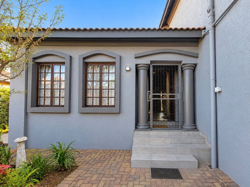 A well-maintained front entrance featuring decorative columns, tiled steps, and timber-framed windows, set against a paved walkway.