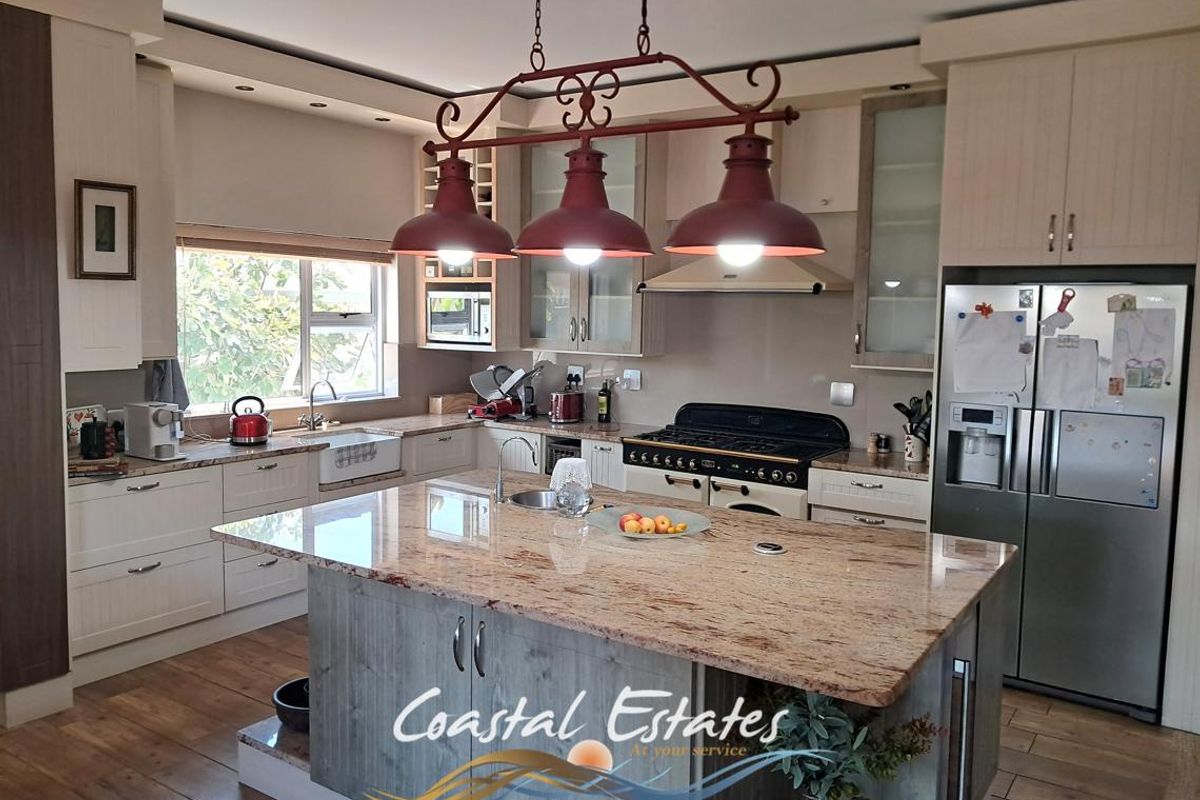 Spacious kitchen featuring a large granite-topped island, custom cabinetry, integrated appliances, and a farmhouse-style sink, offering a functional and well-appointed culinary space.