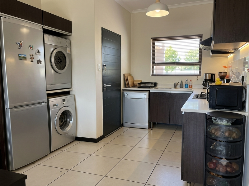 A modern, well-maintained kitchen featuring dark wood cabinetry, stone countertops, tiled flooring, and integrated appliances, including a dedicated laundry area with stacked washer and dryer.
