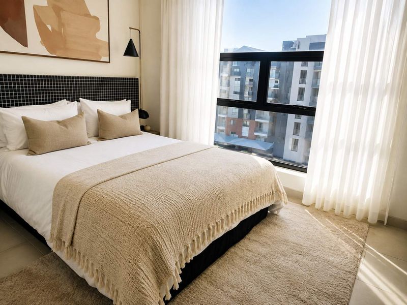 A well-lit bedroom featuring tiled flooring, a modern black-framed window, and a stylish built-in headboard, offering a clean and contemporary living space.