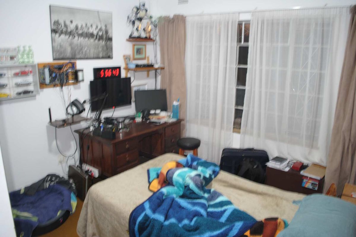 A functional bedroom featuring a window with security burglar bars and curtain rails, providing a basic living space.