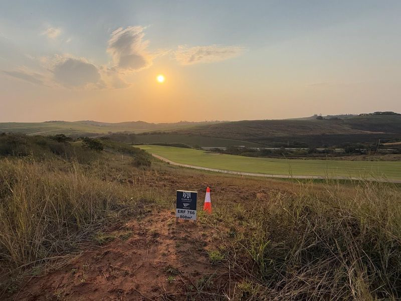 A scenic view of an undeveloped residential plot at sunset, showcasing the natural landscape and surrounding terrain.