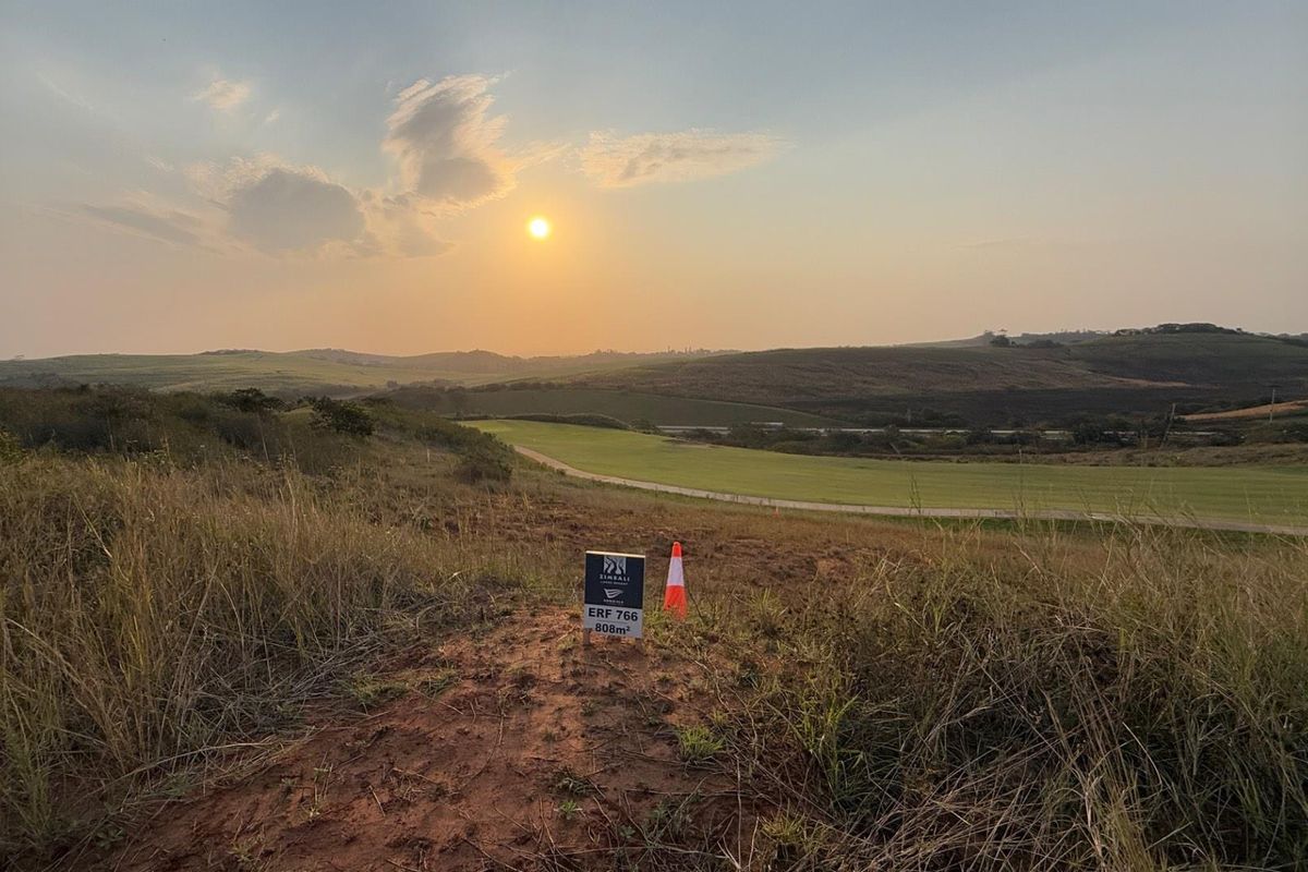 A scenic view of an undeveloped residential plot at sunset, showcasing the natural landscape and surrounding terrain.