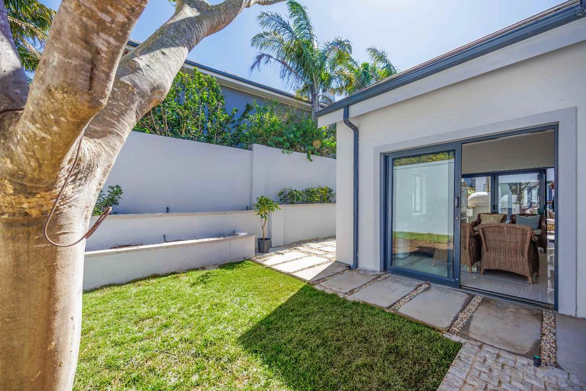 A well-maintained rear garden area featuring a paved walkway, manicured lawn, and a modern sliding glass door providing access to the interior living space.