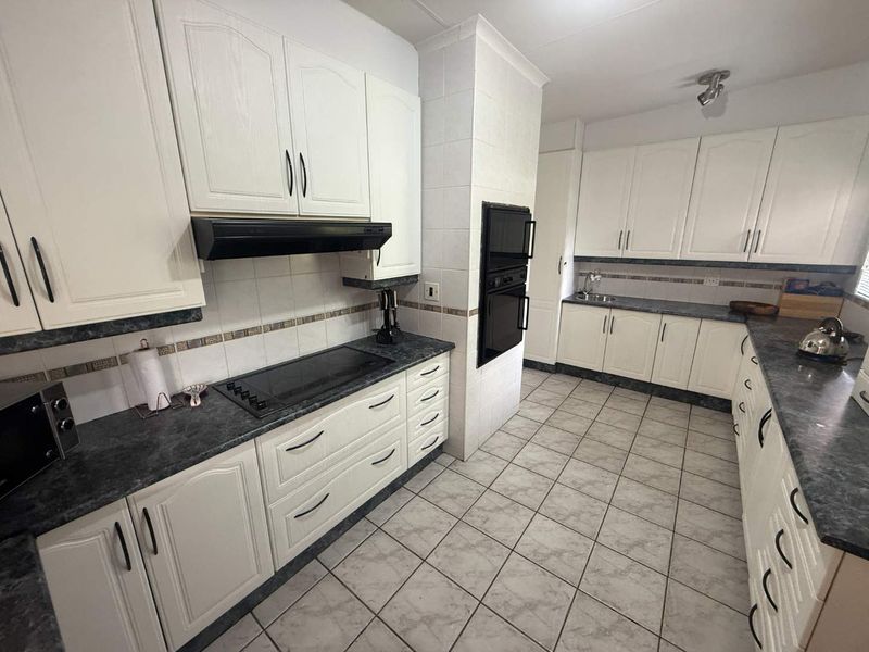 A functional kitchen featuring white cabinetry, dark laminate countertops, tiled flooring, and built-in appliances including an oven and electric cooktop.