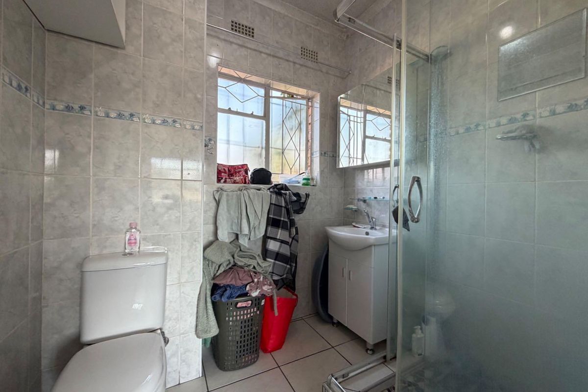 A functional bathroom featuring ceramic wall and floor tiles, a glass shower enclosure, a pedestal vanity, and a medicine cabinet.