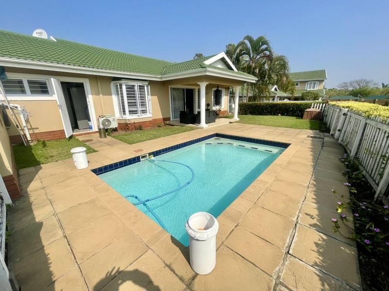 Rear exterior view of the townhouse featuring a private swimming pool, paved surround, covered patio area, and established garden boundary.