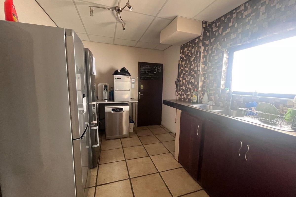 A functional kitchen area featuring dark cabinetry, tiled flooring, a stainless steel sink, and a mosaic-tiled backsplash.