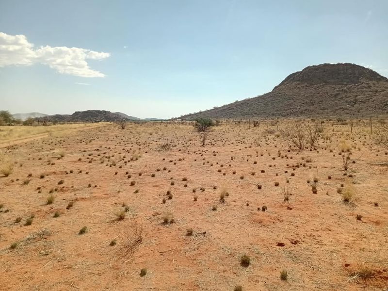 A wide-angle view of open agricultural land featuring arid terrain, sparse vegetation, and distant mountain ranges under a clear sky.