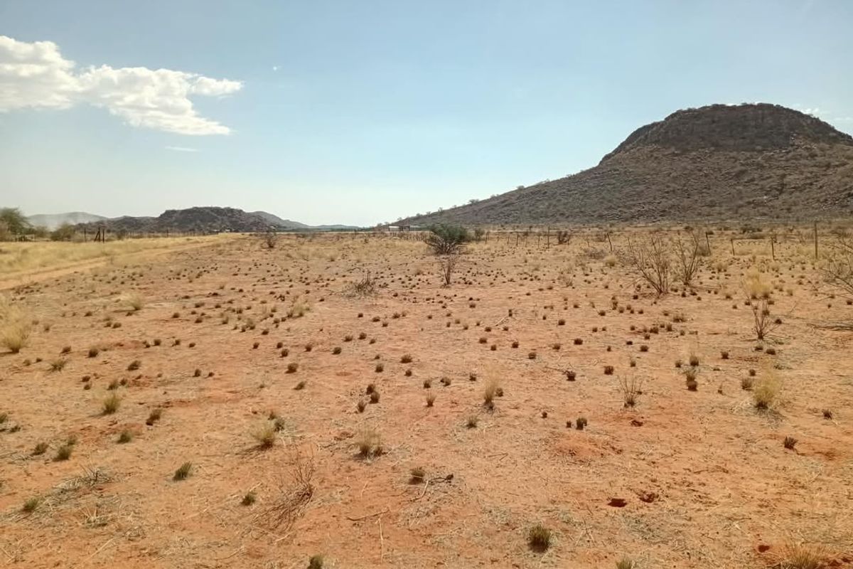 A wide-angle view of open agricultural land featuring arid terrain, sparse vegetation, and distant mountain ranges under a clear sky.