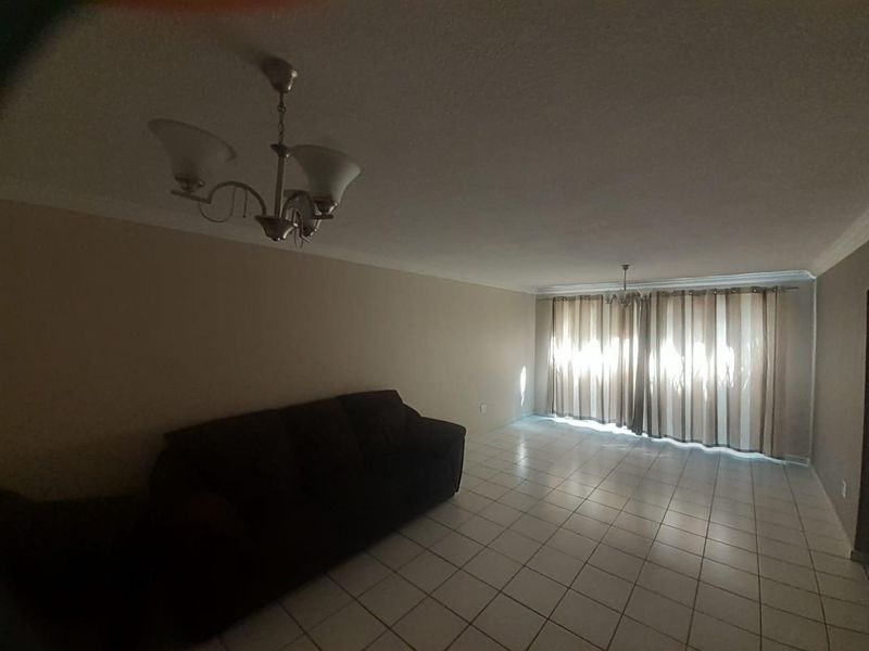 Spacious living room featuring neutral tiled flooring, coved cornicing, and large windows with curtains, offering a blank canvas for interior design.