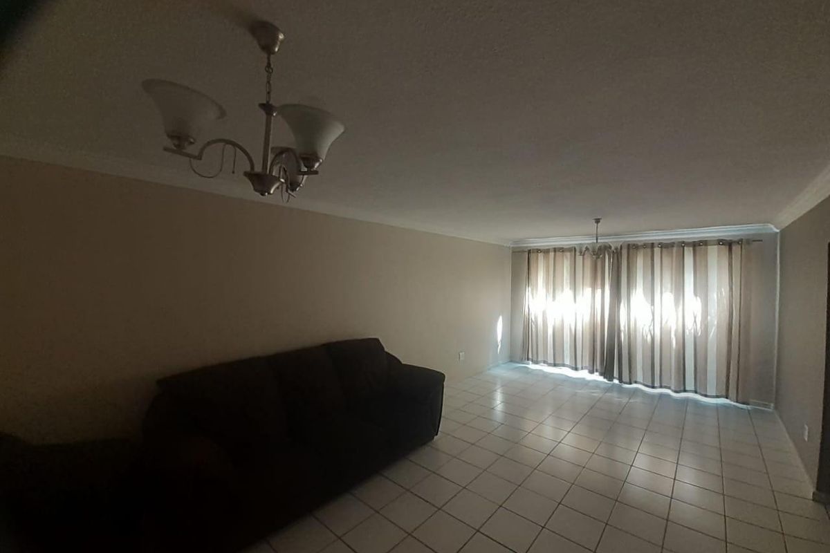Spacious living room featuring neutral tiled flooring, coved cornicing, and large windows with curtains, offering a blank canvas for interior design.