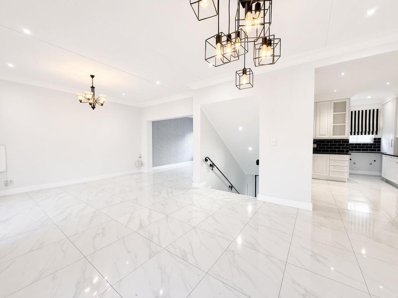 Spacious open-plan living area featuring polished marble-look floor tiles, modern lighting fixtures, and a seamless transition to the kitchen and staircase.
