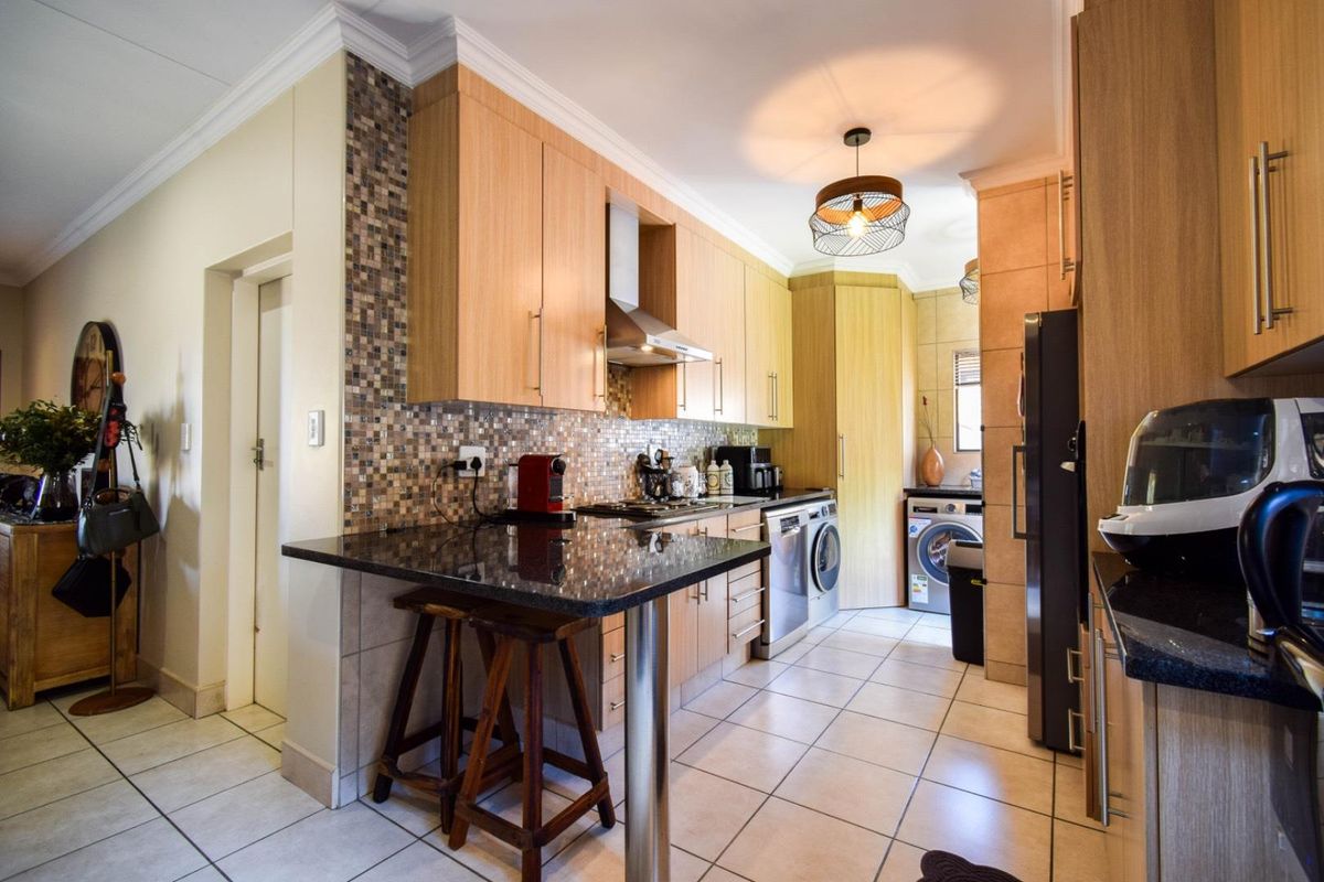 A functional kitchen featuring light wood cabinetry, granite countertops, mosaic tile backsplash, and integrated laundry appliances.