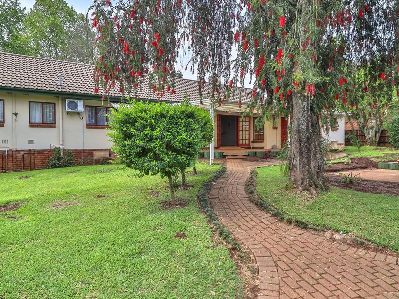 Rear view of the house featuring a brick pathway leading to a covered entrance, set within a landscaped garden with mature trees.