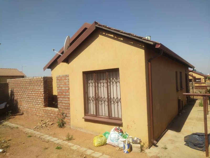 Rear view of a detached house featuring a tiled roof, security gate, and unfinished brick boundary wall in a residential setting.