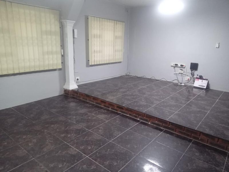 An empty living area featuring a raised tiled platform, decorative column, and vertical blinds. The space requires minor repairs to exposed wiring and brickwork.