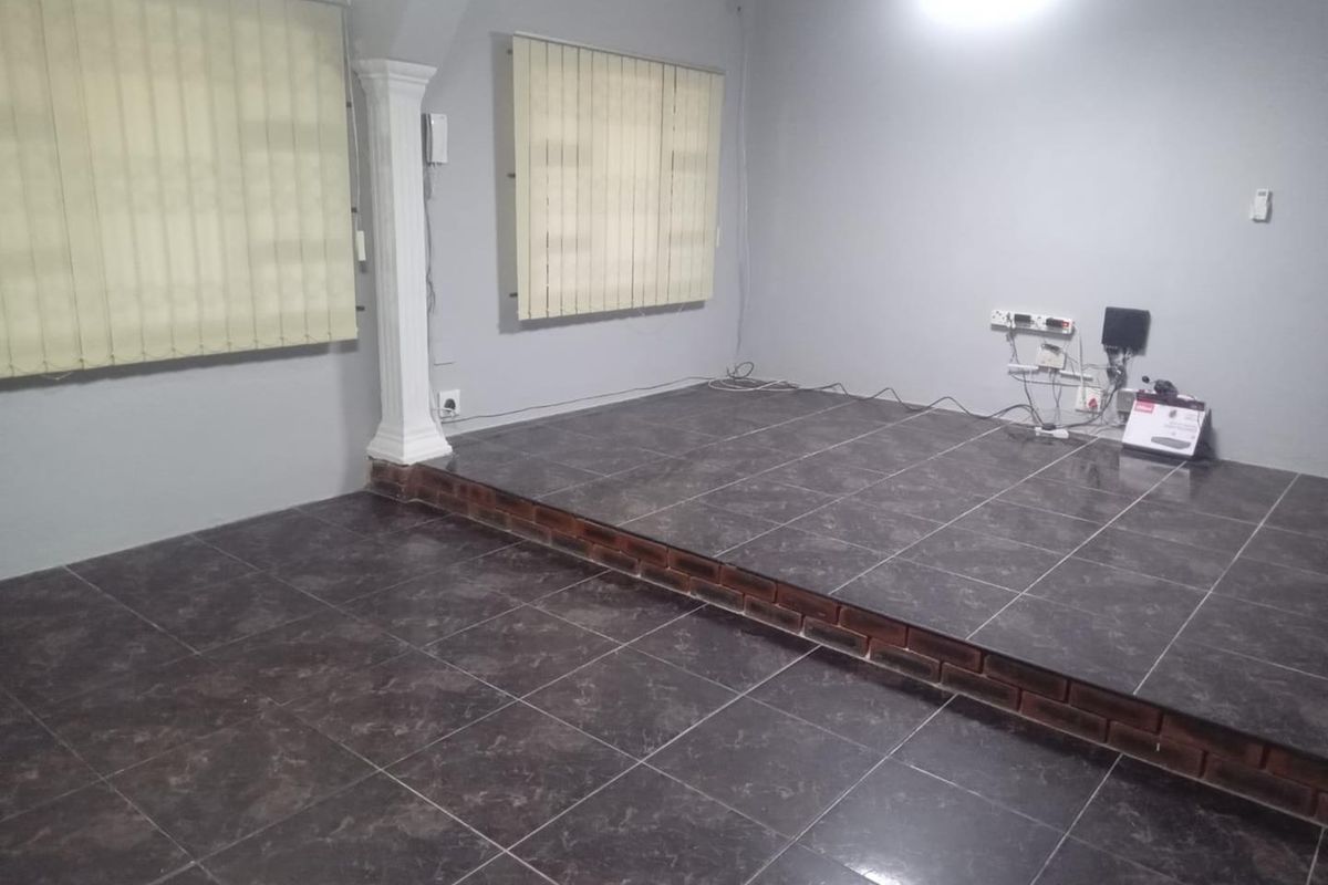 An empty living area featuring a raised tiled platform, decorative column, and vertical blinds. The space requires minor repairs to exposed wiring and brickwork.