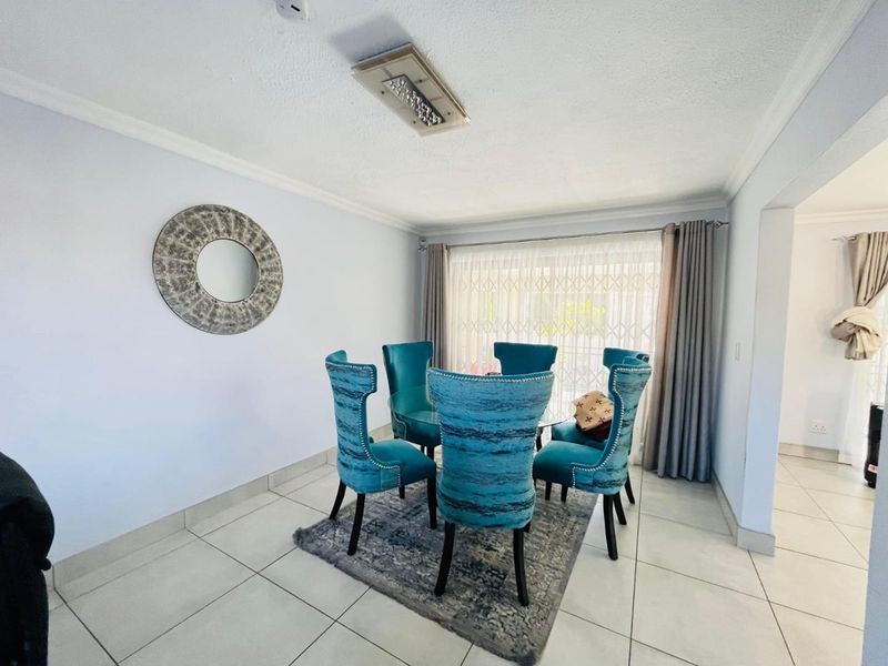 A bright dining room featuring neutral tiled flooring, a ceiling-mounted light fixture, and a sliding glass door with security gate access to the exterior.
