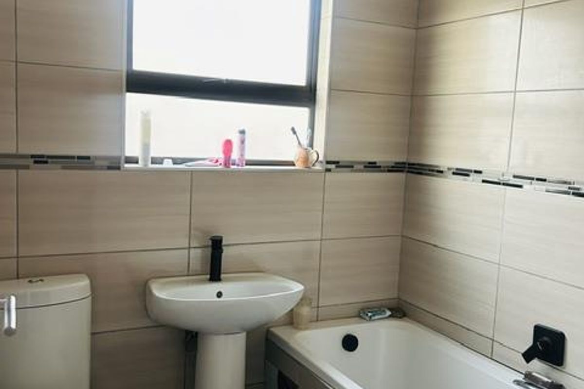 A modern bathroom featuring neutral wall tiles, a pedestal basin, a bathtub with black fixtures, and a toilet.