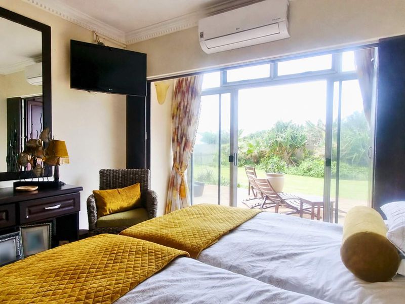 A well-lit bedroom featuring large sliding glass doors that provide direct access to the garden, complemented by a wall-mounted air conditioning unit.