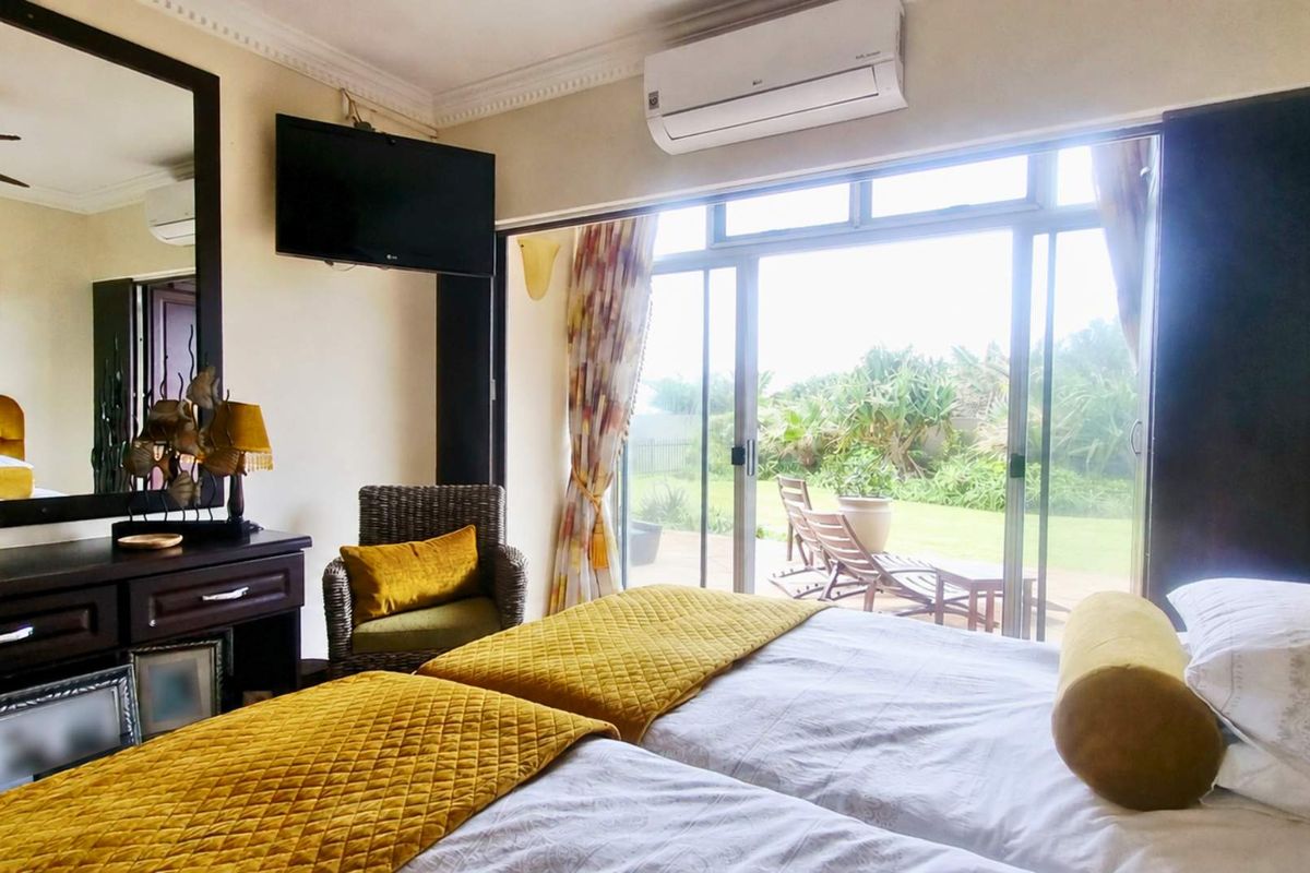 A well-lit bedroom featuring large sliding glass doors that provide direct access to the garden, complemented by a wall-mounted air conditioning unit.