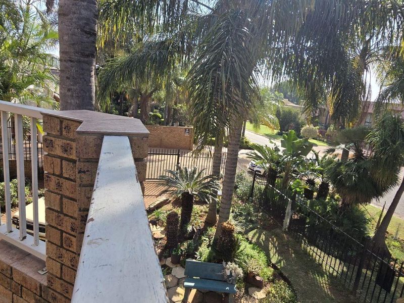 An elevated balcony featuring a brick and metal balustrade, overlooking a landscaped garden and street view.