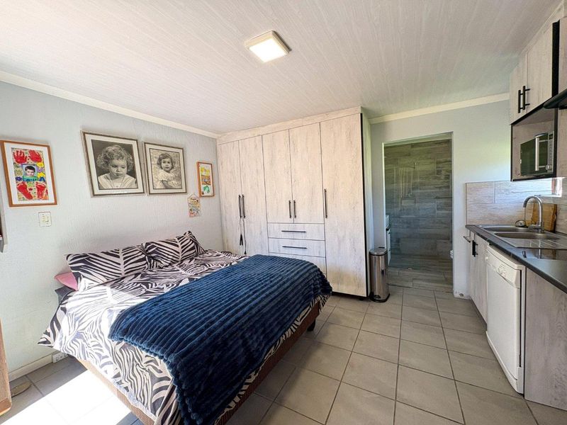 Open-plan bedroom featuring built-in storage cupboards, a compact kitchenette with sink, and direct access to an en-suite bathroom with tiled finishes.