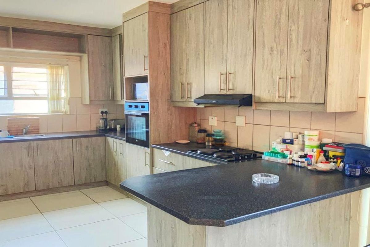 A functional kitchen featuring wood-look cabinetry, dark laminate countertops, built-in oven, hob, extractor fan, and tiled flooring with a neutral backsplash.