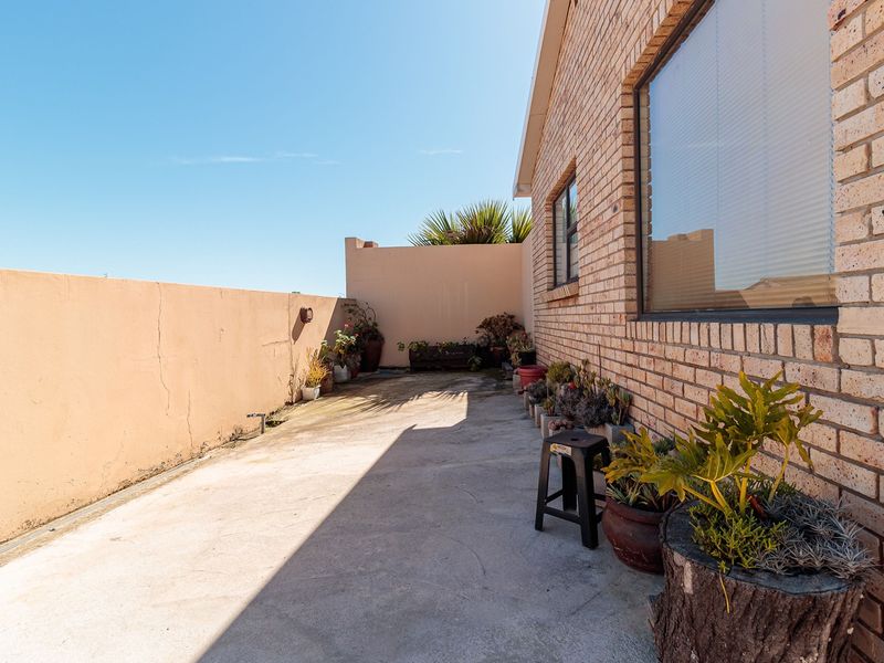 A rear exterior view featuring a concrete patio area adjacent to a face brick wall and a boundary wall with visible surface cracks.