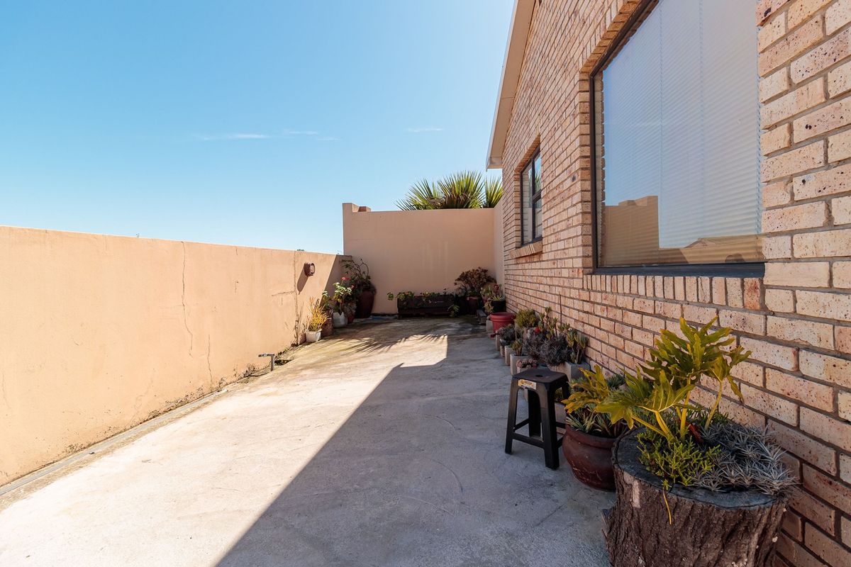 A rear exterior view featuring a concrete patio area adjacent to a face brick wall and a boundary wall with visible surface cracks.