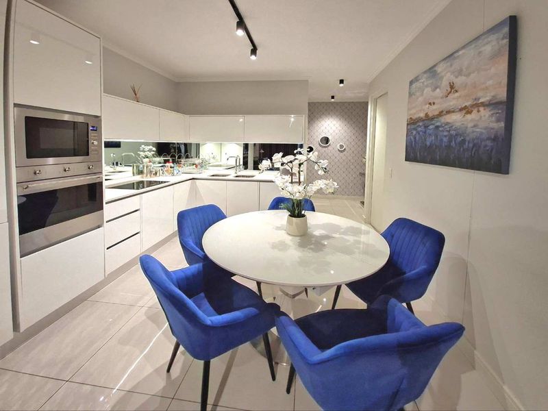 Modern open-plan kitchen and dining area featuring sleek white cabinetry, integrated appliances, mirror splashback, and contemporary track lighting.