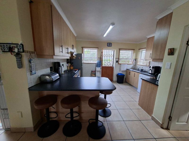 Functional kitchen featuring light wood cabinetry, dark laminate countertops, tiled flooring, and a breakfast bar area with direct access to the exterior.
