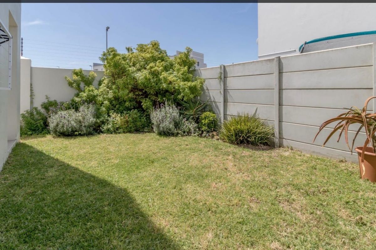 A private rear garden featuring a lawn, established shrubs, and a precast concrete boundary wall with a wall-mounted washing line.