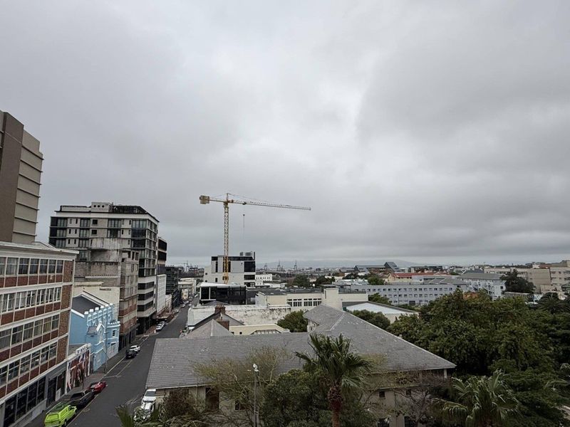 An elevated urban view overlooking surrounding city buildings, streets, and a construction crane under a cloudy sky.
