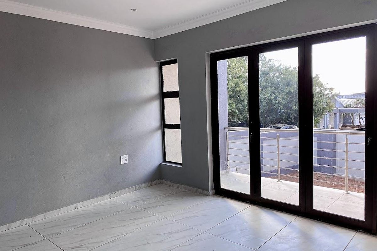 A bright, empty living room featuring modern marble-look floor tiles, grey walls, and large glass sliding doors opening onto a private balcony.