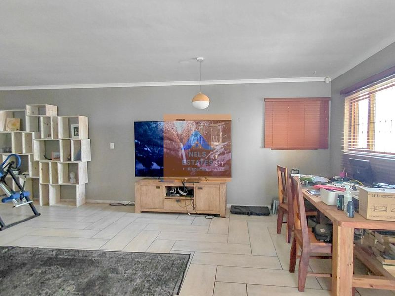 Spacious living room featuring neutral grey walls, tiled flooring, and large windows with venetian blinds, offering a versatile layout for relaxation.
