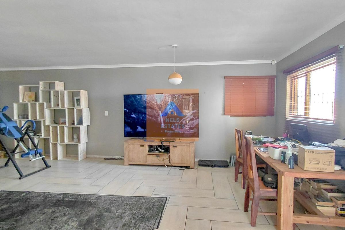 Spacious living room featuring neutral grey walls, tiled flooring, and large windows with venetian blinds, offering a versatile layout for relaxation.
