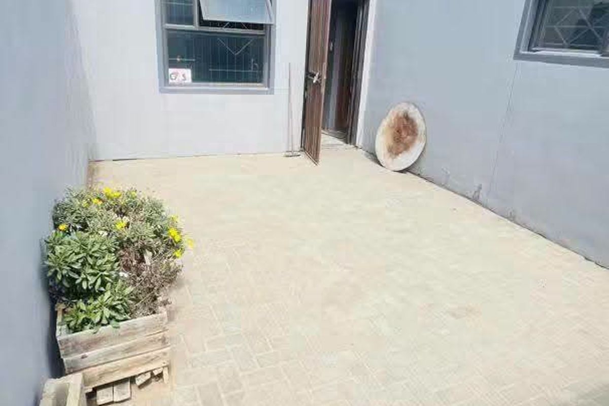 A private paved rear courtyard area featuring high boundary walls, security gate access, and external lighting.