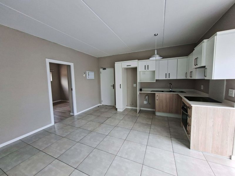 An open-plan kitchen area featuring modern two-tone cabinetry, tiled flooring, and integrated appliances, offering a clean and functional space.