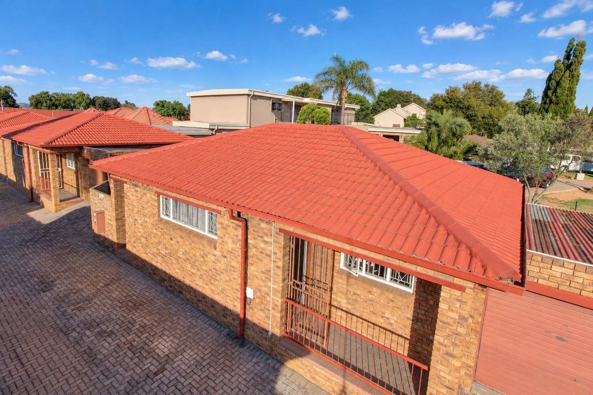 Aerial view of a townhouse complex featuring facebrick construction, red tiled roofs, and paved driveway access.