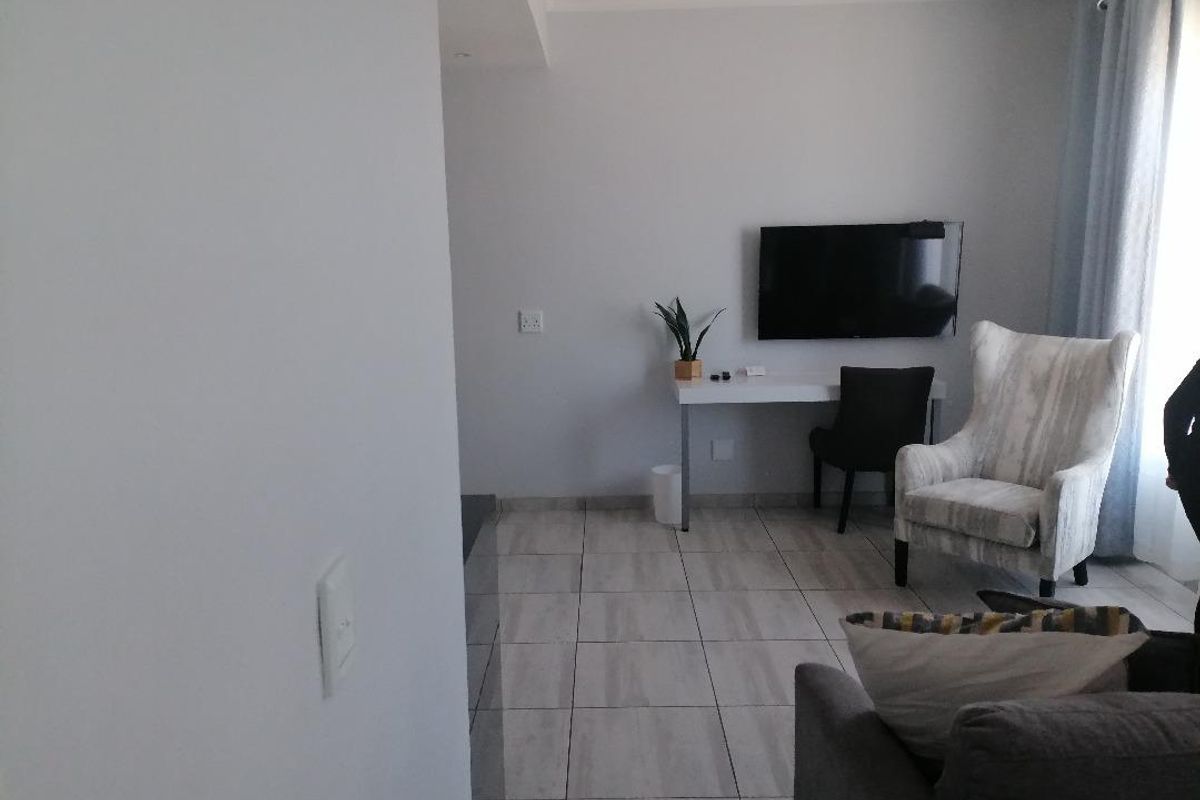 A functional hotel room featuring tiled flooring, a wall-mounted television, and a built-in desk area.
