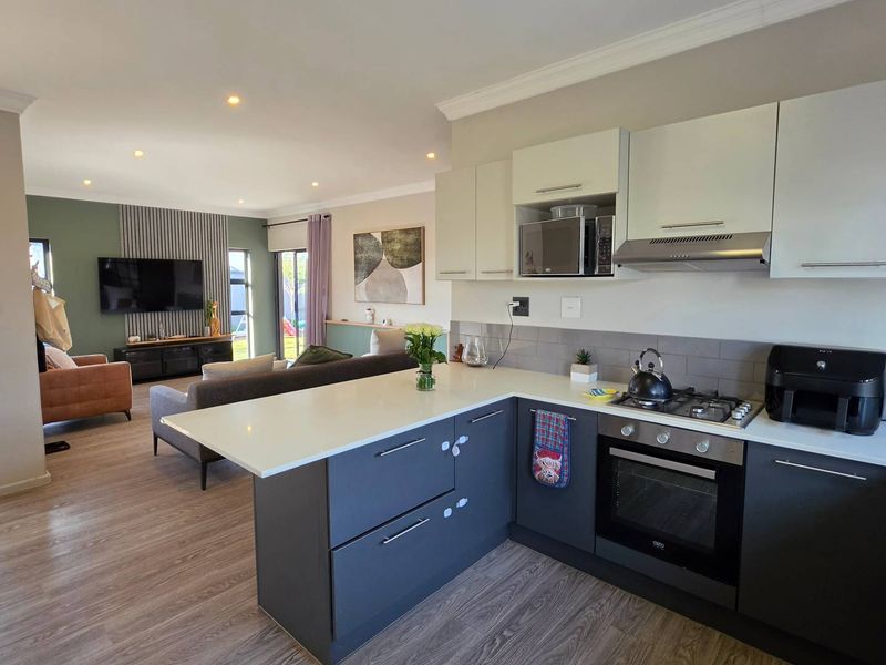 Modern open-plan kitchen and living area featuring contemporary two-tone cabinetry, stone countertops, integrated appliances, and durable laminate flooring throughout the space.