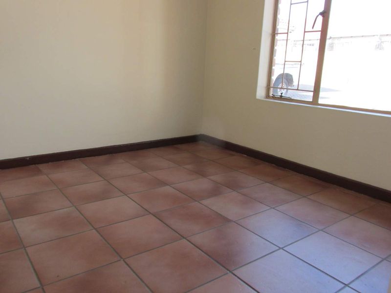 An empty bedroom featuring terracotta-style floor tiles, neutral walls, and a window fitted with security bars.