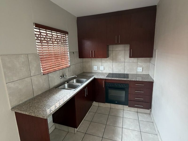 A clean and functional kitchen featuring dark wood cabinetry, granite countertops, a built-in oven with hob, and neutral ceramic floor tiles.