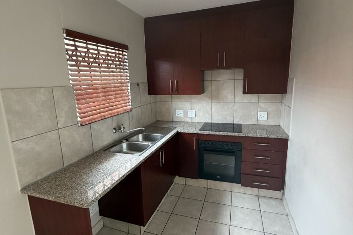 A clean and functional kitchen featuring dark wood cabinetry, granite countertops, a built-in oven with hob, and neutral ceramic floor tiles.