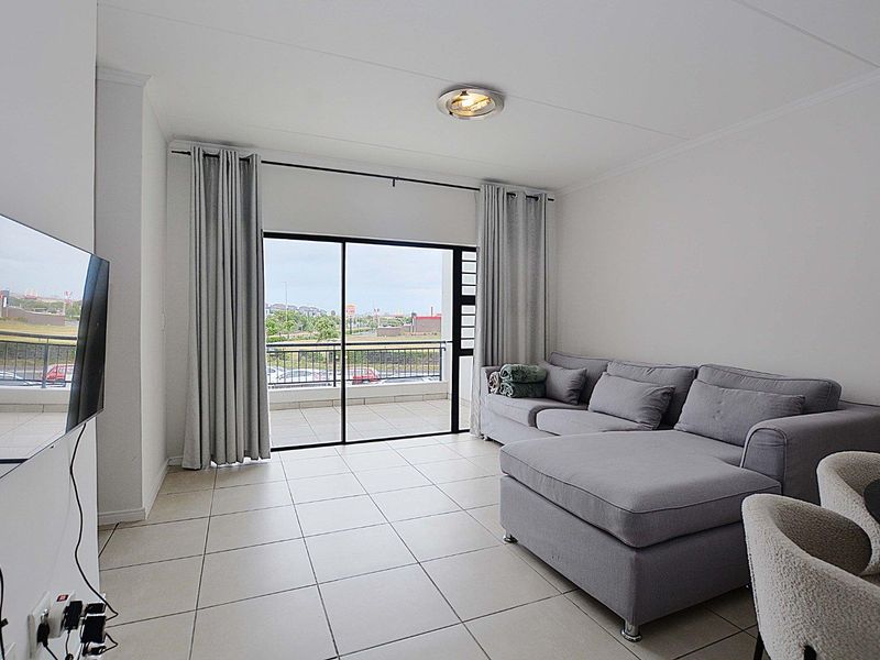 A bright living room featuring neutral tiled flooring and a large sliding glass door providing direct access to an outdoor balcony.
