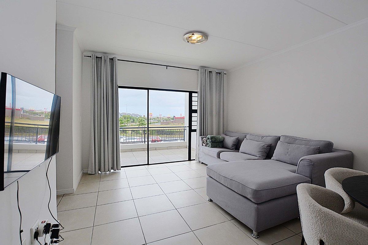 A bright living room featuring neutral tiled flooring and a large sliding glass door providing direct access to an outdoor balcony.