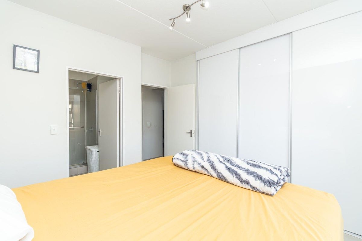 A bright bedroom featuring built-in sliding door wardrobes and an en-suite bathroom with a glass-enclosed shower.